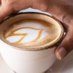 5G Technology - A person's hand holding a cup of coffee with a laptop in the background