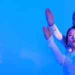 AI Models - Young Man and Woman in Futuristic Clothing Standing in a Studio with Blue Lighting and Holding Their Arms Up