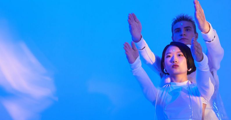 AI Models - Young Man and Woman in Futuristic Clothing Standing in a Studio with Blue Lighting and Holding Their Arms Up