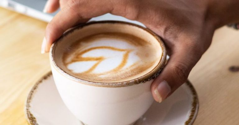 5G Technology - A person's hand holding a cup of coffee with a laptop in the background